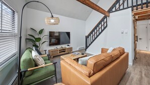 Una sala de estar con un sillón verde, un sofá marrón, una mesa de centro de madera y un televisor en la pared.