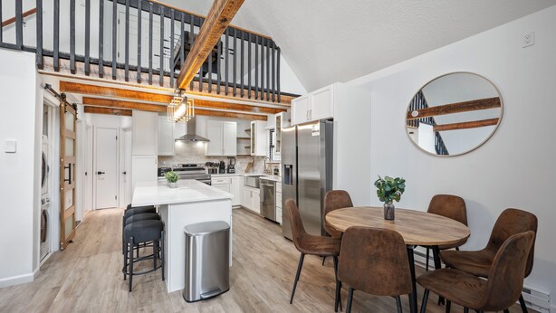 Una cocina moderna con armarios blancos, un refrigerador de acero inoxidable y una mesa de comedor de madera con sillas marrones.