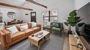 Una sala de estar moderna con un sofá de cuero marrón, sillones verdes y una mesa de centro de madera.