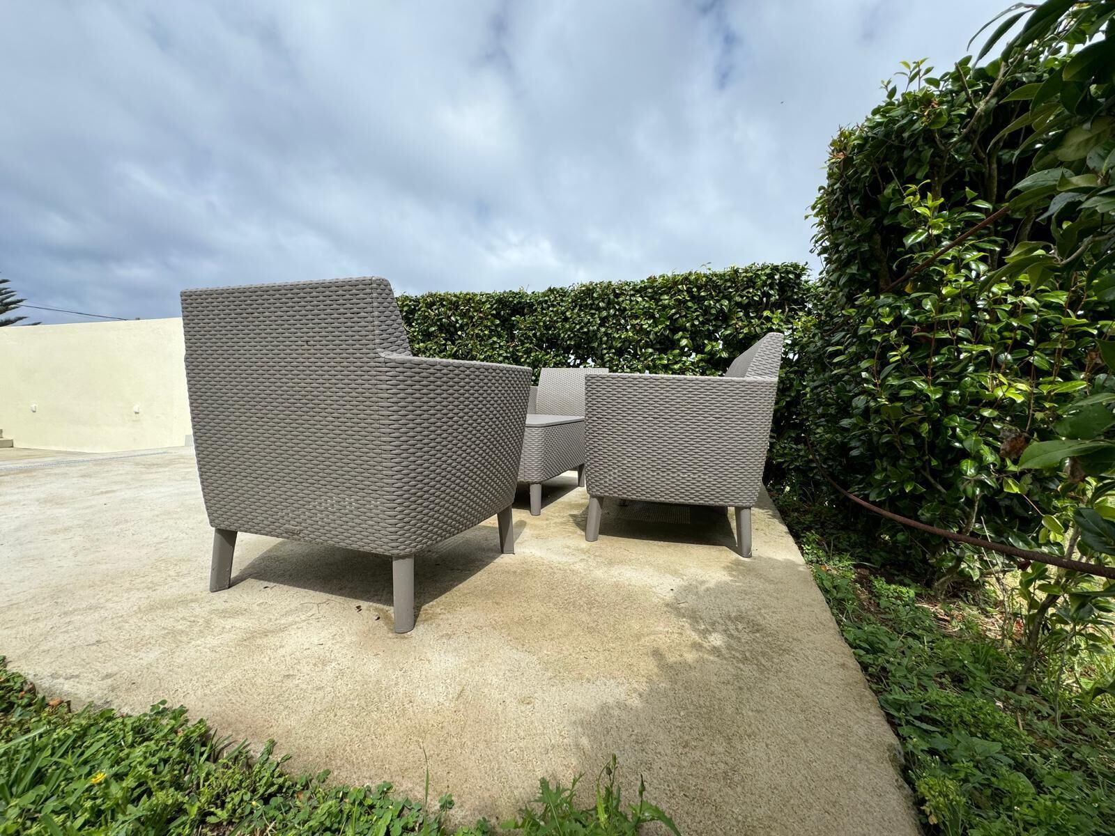 Eine Terrasse mit zwei grauen Korbstühlen und einem kleinen Tisch.