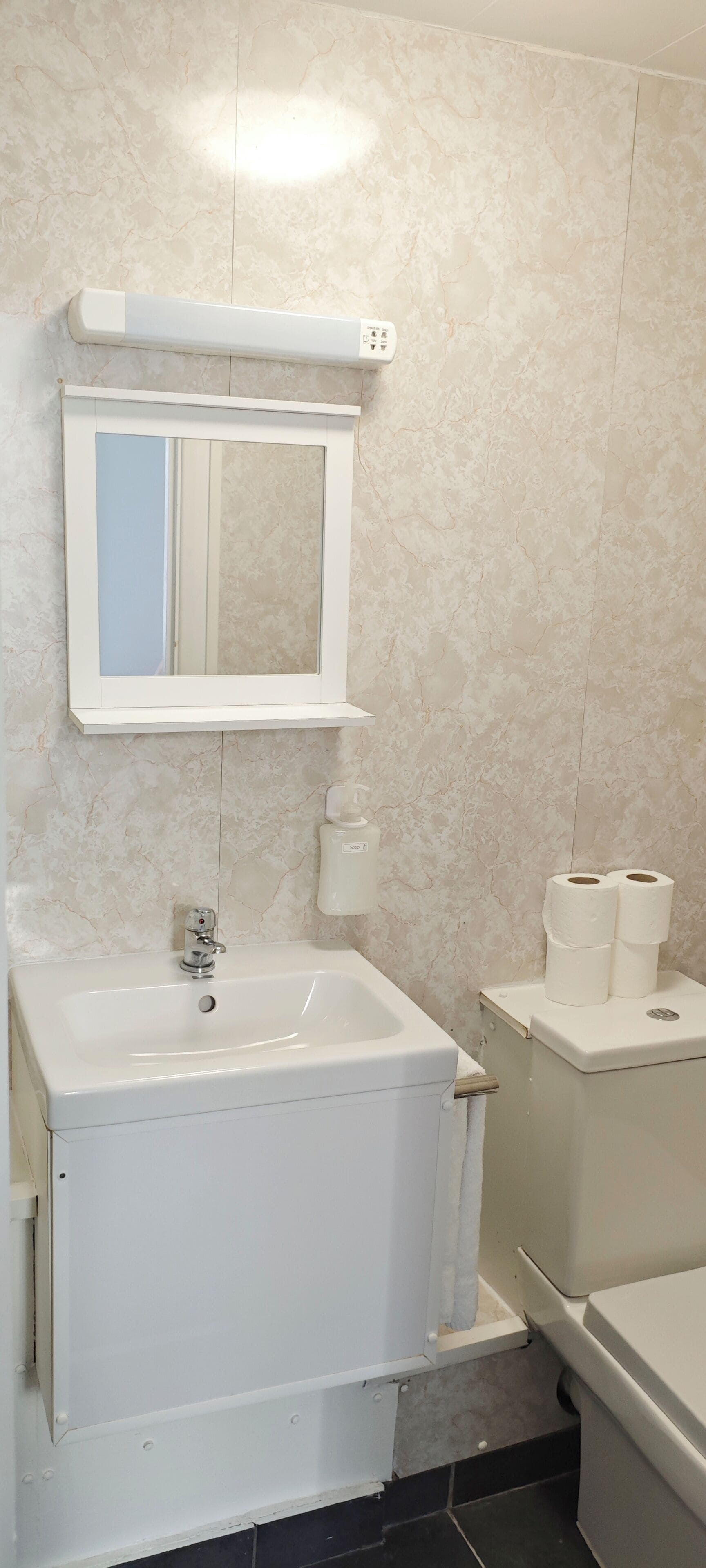A bathroom with a white sink, a mirror, a toilet, and a trash bin.