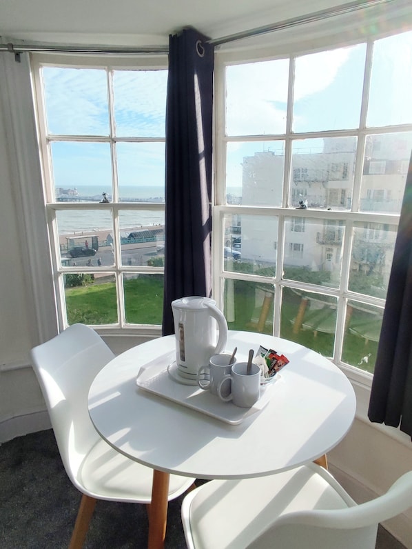 Une pièce avec une table blanche, deux chaises blanches, une bouilloire blanche, deux tasses blanches et un plateau avec une cuillère et un petit récipient.