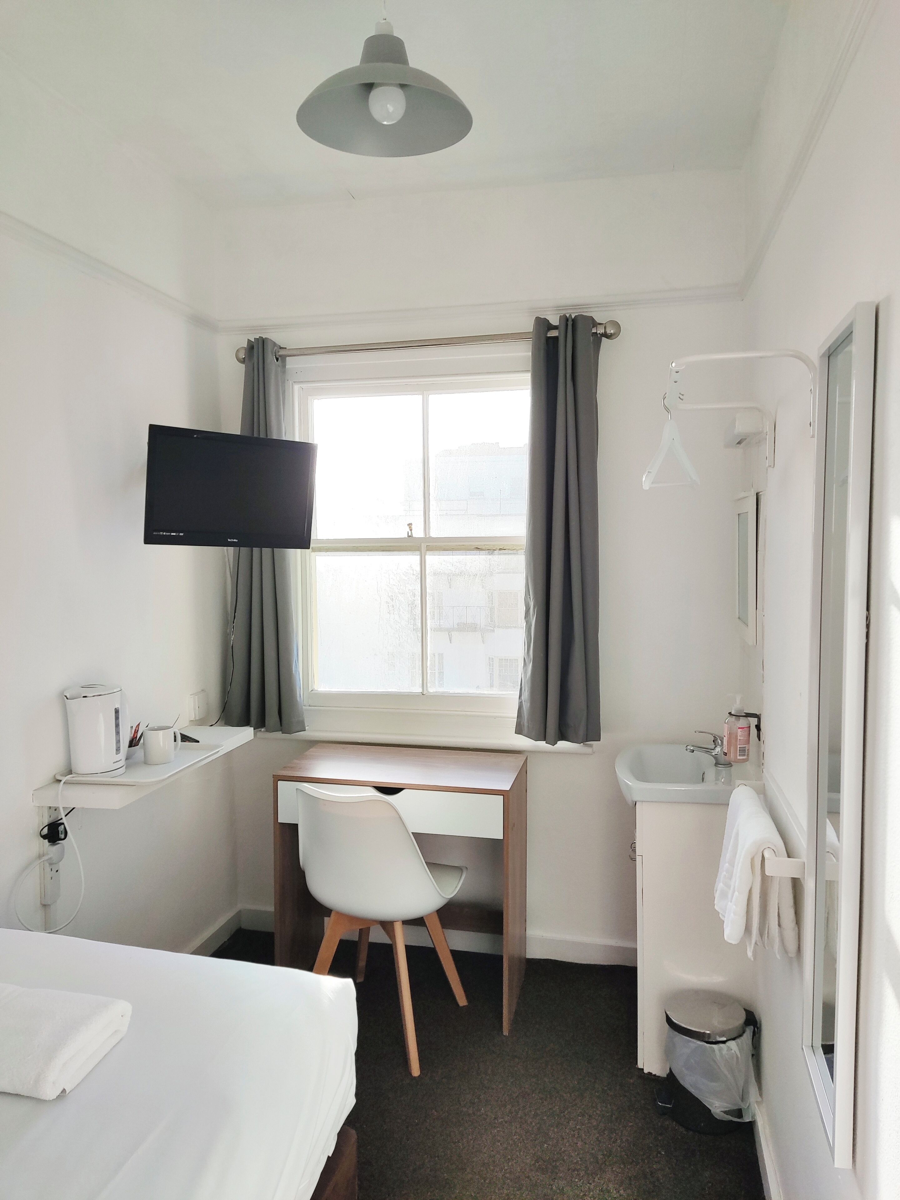 Hotellihuone, jossa on sänky, työpöytä, televisio, ikkuna verhoilla, pesuallas ja peili.