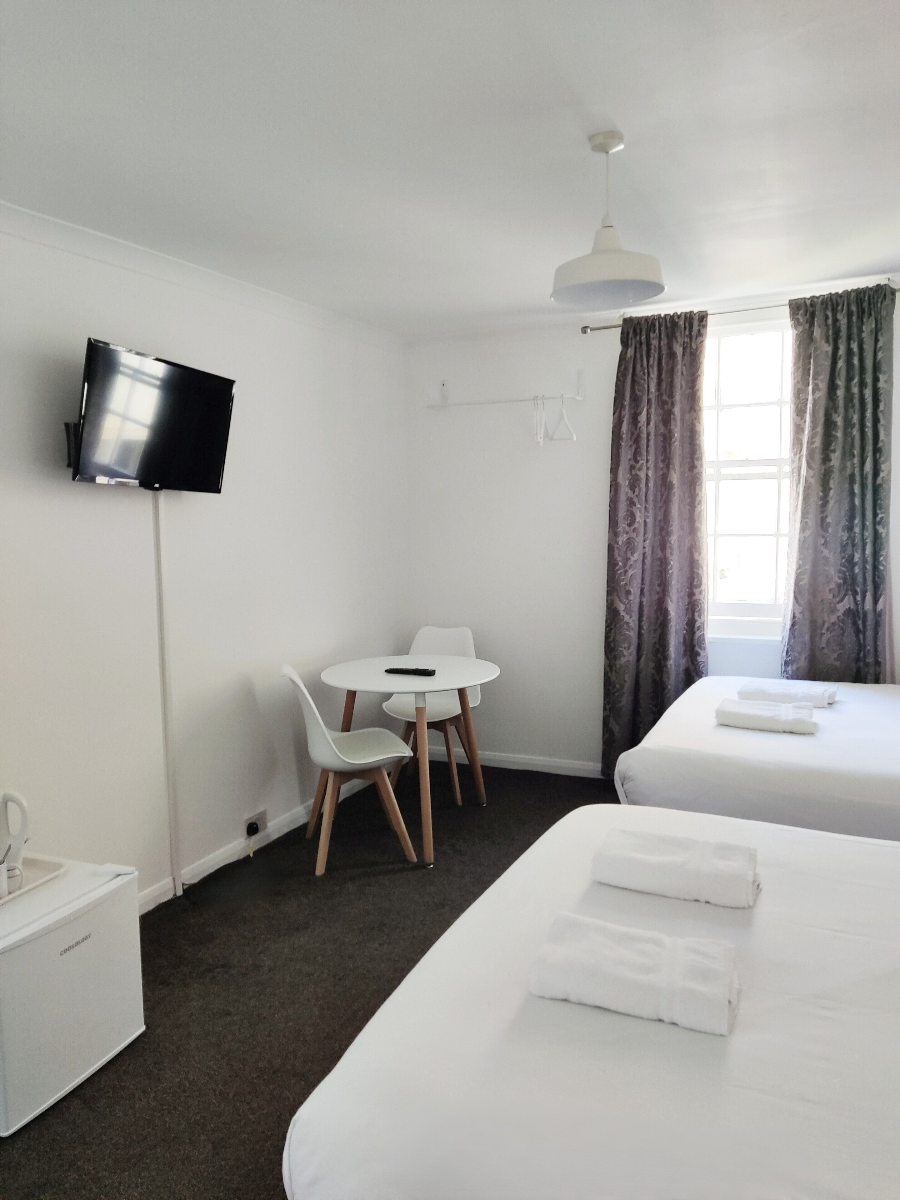 A hotel room with a bed, a desk with a chair, a television mounted on the wall, and a window with curtains.