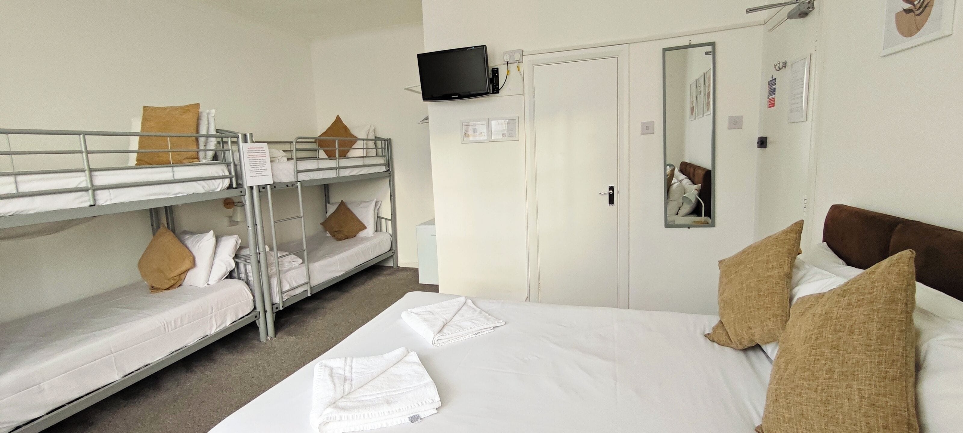 A hotel room with bunk beds, a television, a wardrobe, and a mirror.