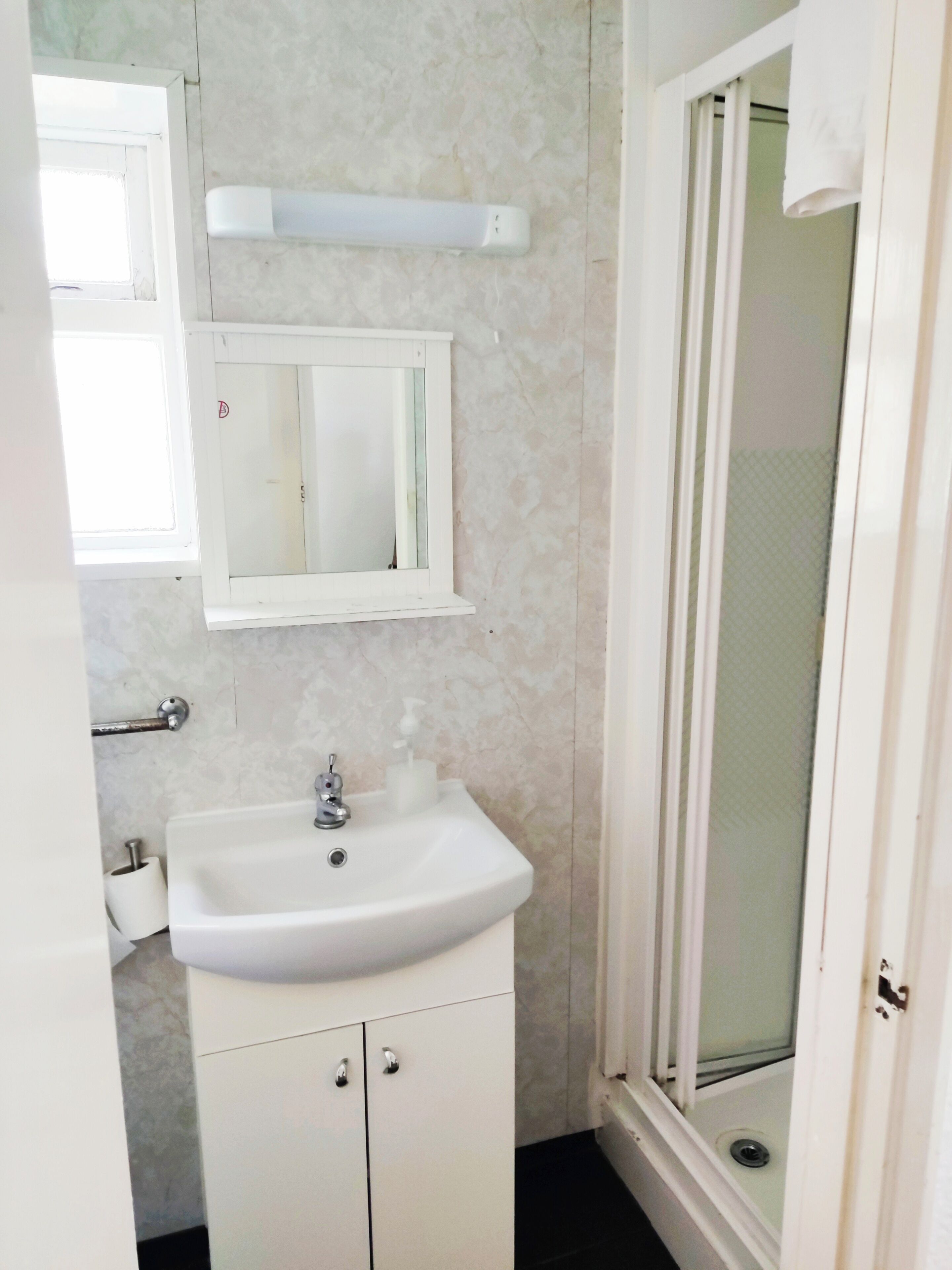 Une salle de bain équipée d’un lavabo, d’un miroir, d’un porte-serviettes et d’une douche.