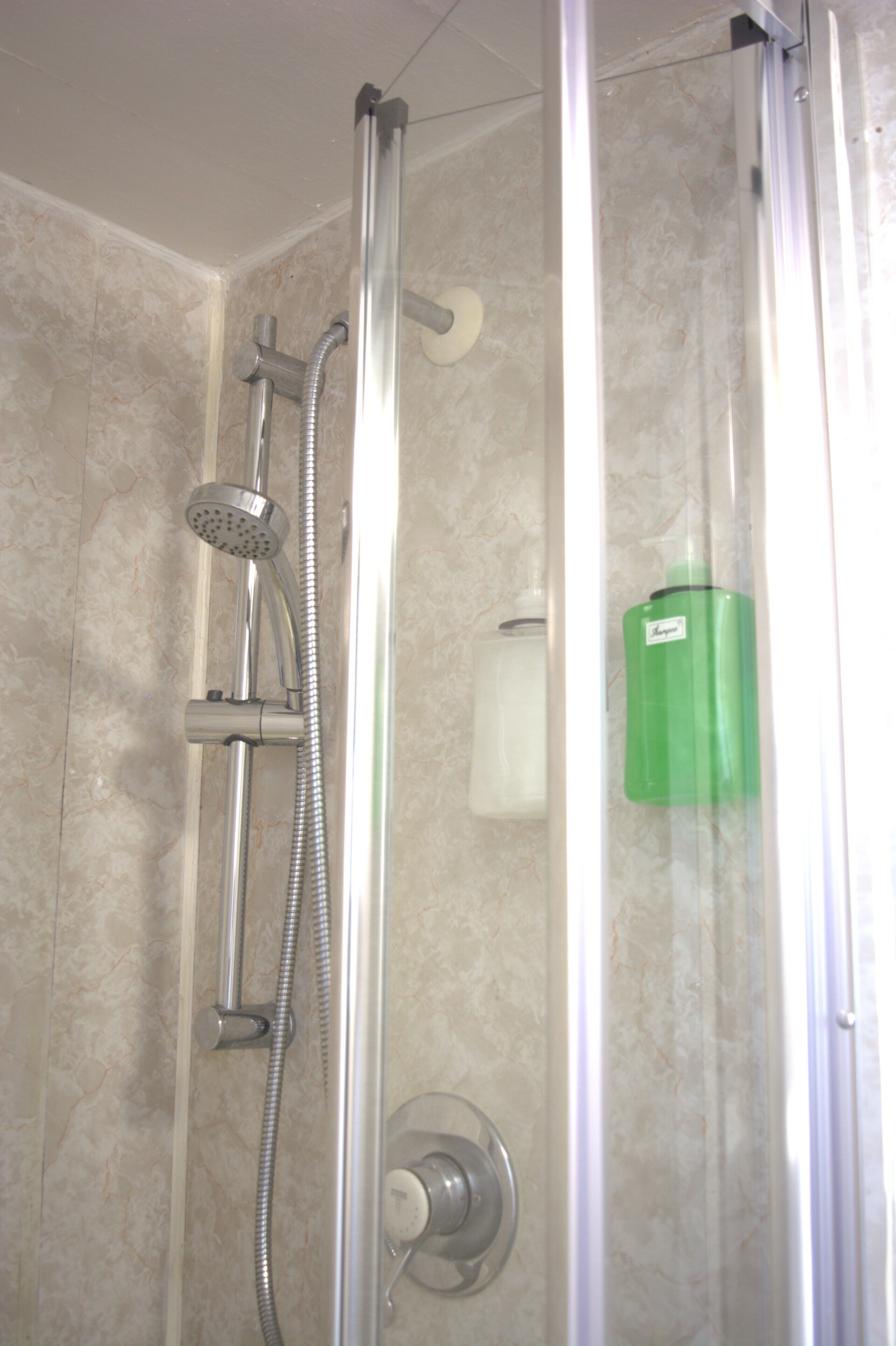 Cabina de ducha con cabezal de ducha de mano, grifo empotrado en la pared y una botella verde de champú.