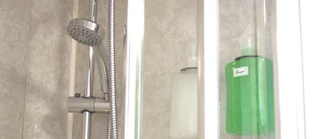 A shower enclosure with a handheld showerhead, a wall-mounted faucet, and a green bottle of shampoo.
