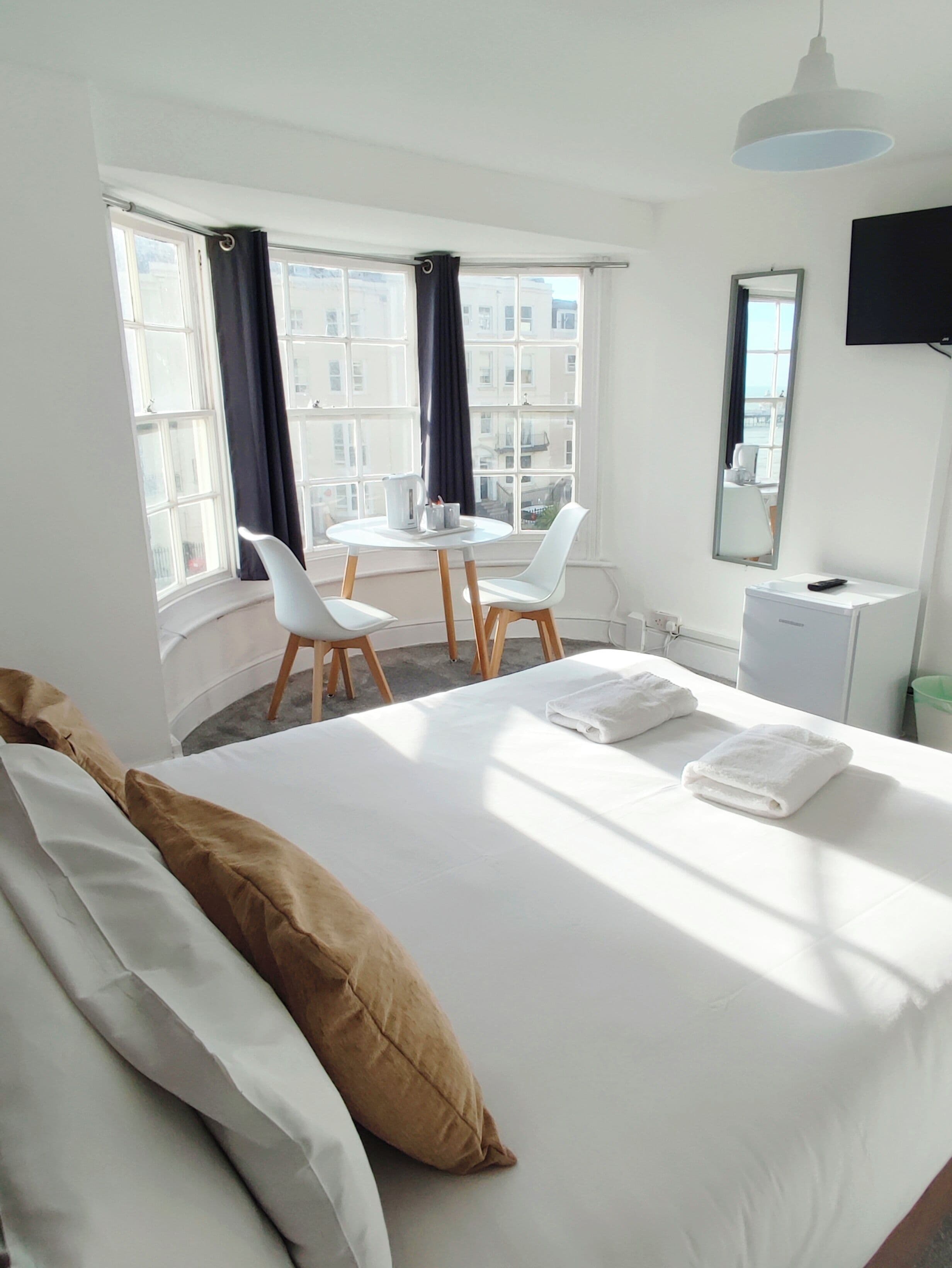 Een hotelkamer met een bed, een tafel met stoelen, een televisie en een raam met gordijnen.