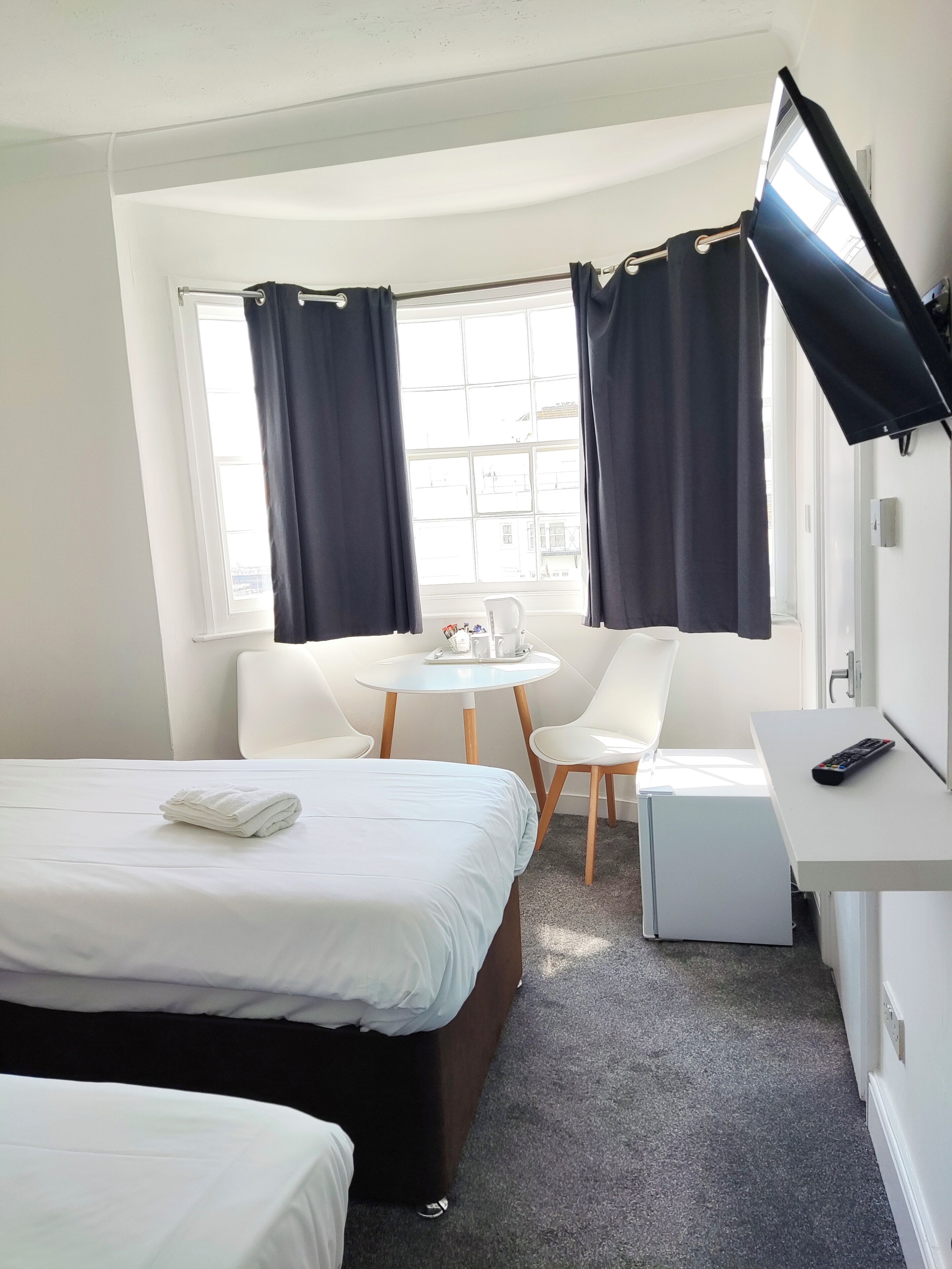 Ein Hotelzimmer mit einem Bett, einem Schreibtisch, einem Stuhl, einem kleinen Tisch mit Tasse und Untertasse sowie einem Fernseher an der Wand.