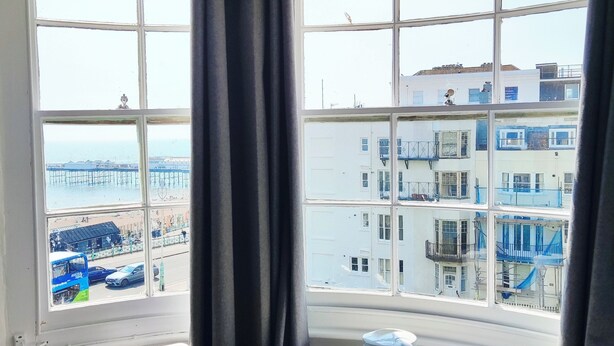 A room with a large window, a table with a tray, and two chairs. - Central Wave Brighton  (Brighton)
