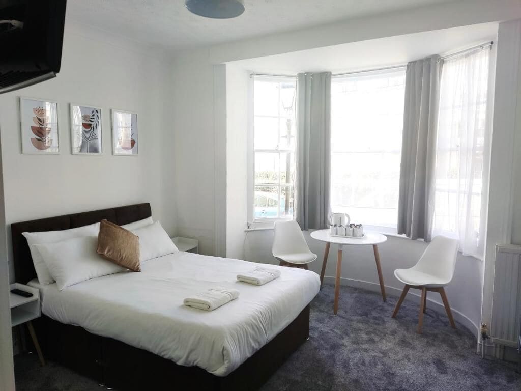 Een hotelkamer met een bed, een ronde tafel met stoelen, een raam met gordijnen en kunst aan de muur.