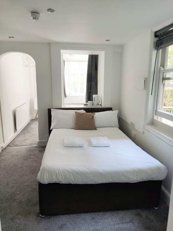 Une chambre d’hôtel avec un grand lit, une fenêtre avec des rideaux, une table de chevet avec une lampe et un radiateur.