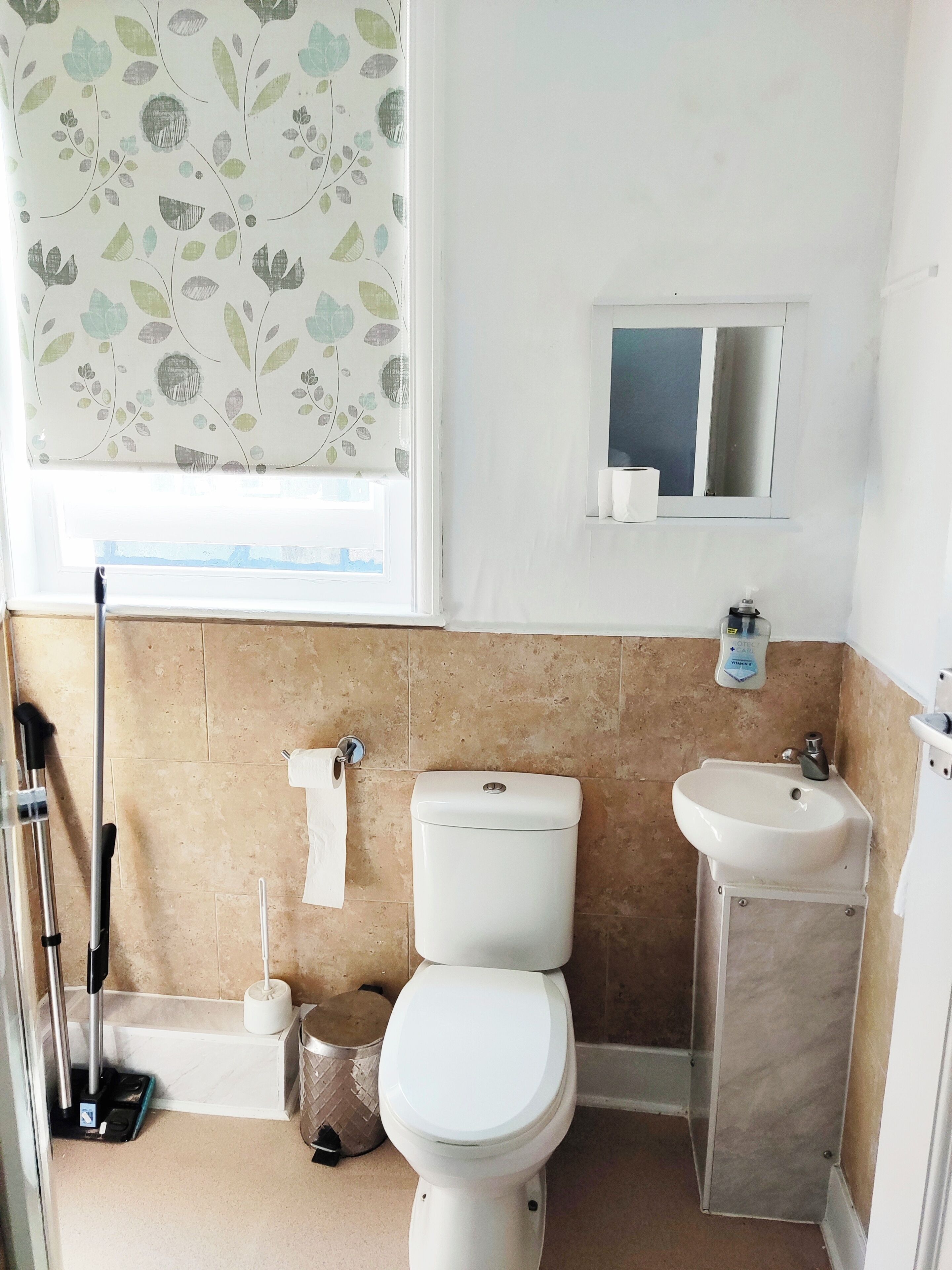 A bathroom with a toilet, sink, and window with floral curtains.