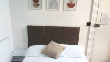A neatly made bed with two towels, a brown pillow, and three framed artworks on the wall.