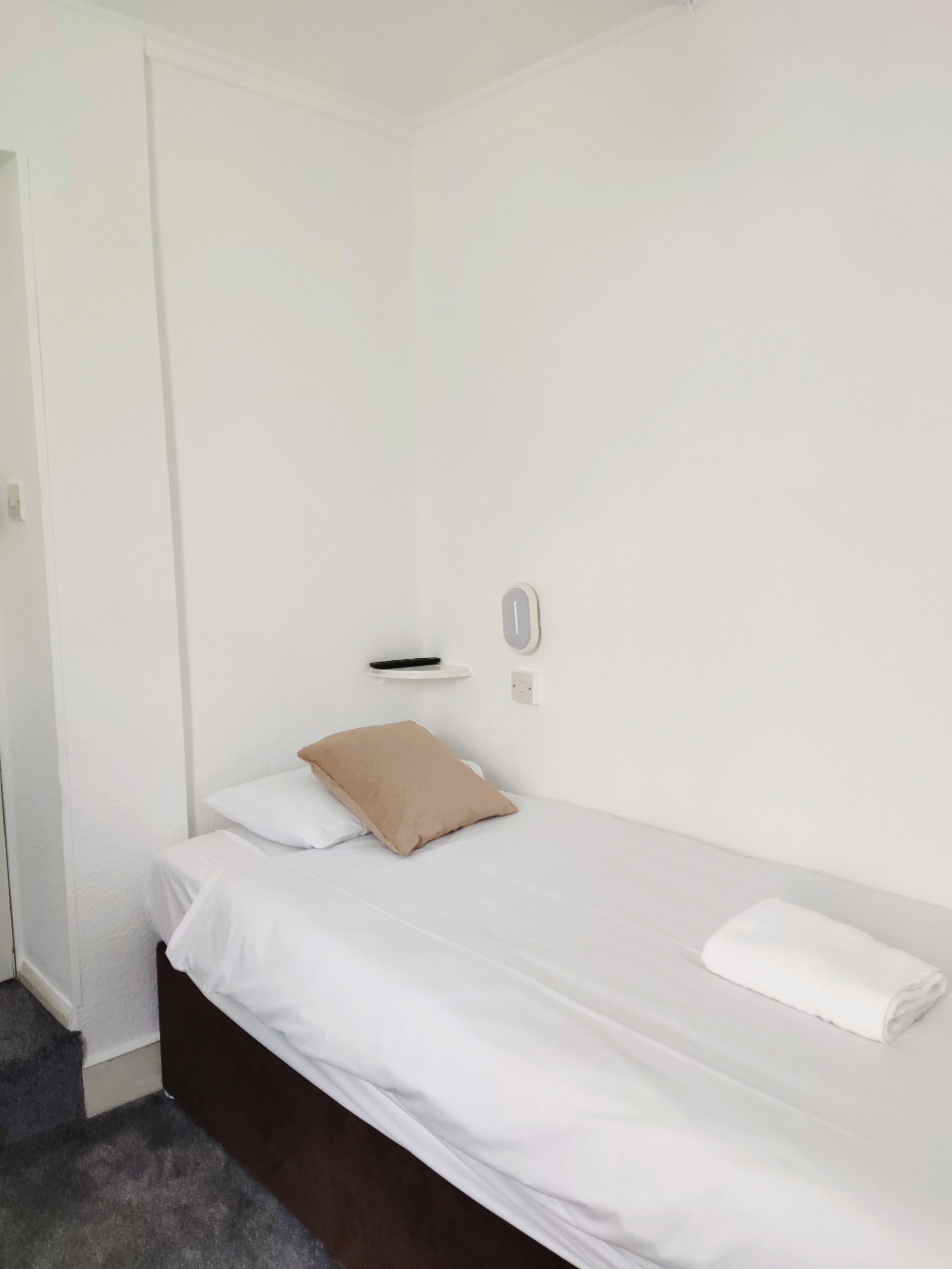 A simple, clean room with a bed, a remote control, and a wall socket.