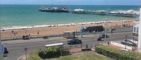 A coastal view with a beach, pier, and parked cars.
