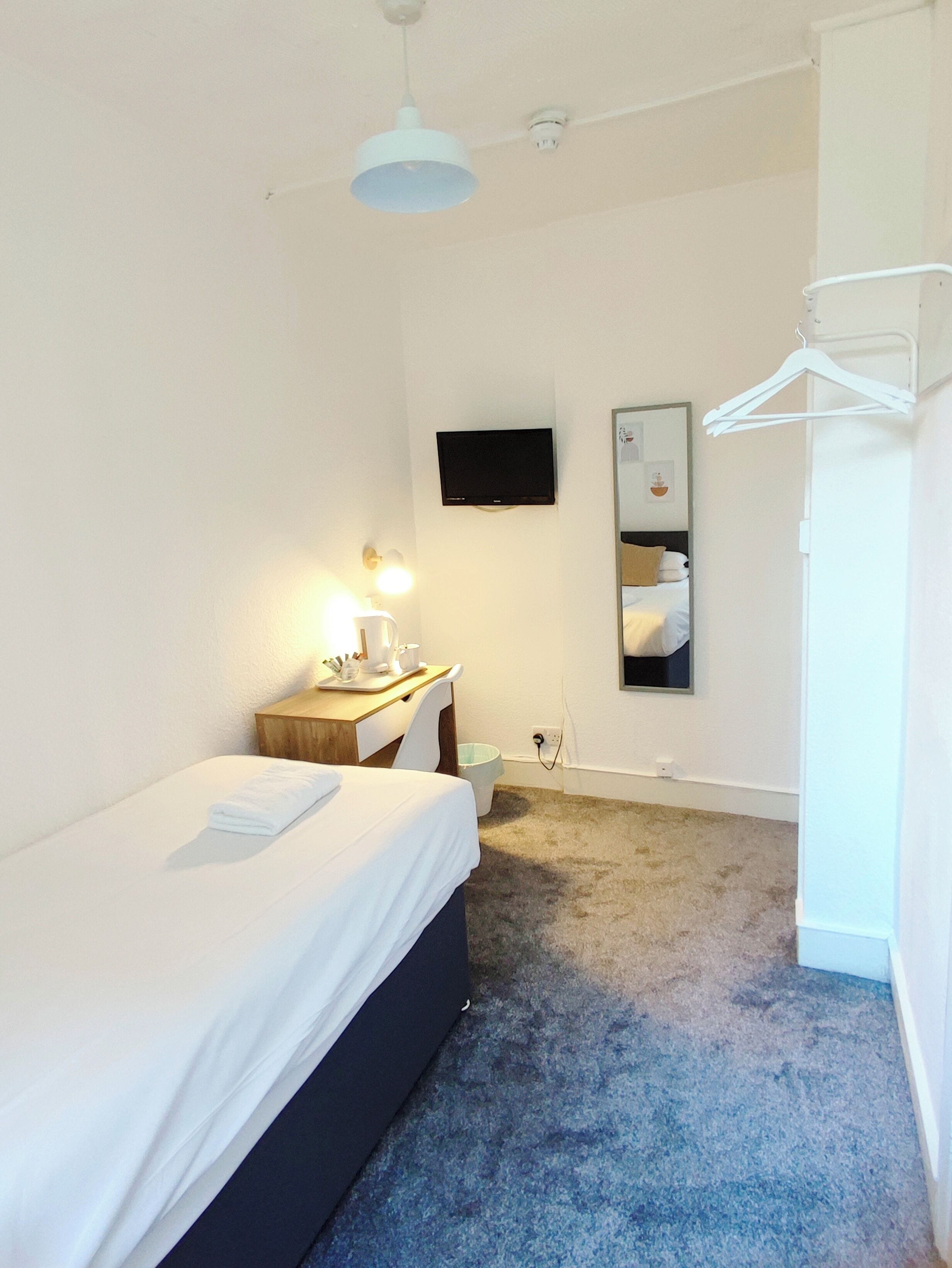 A hotel room with a bed, bedside table, lamp, TV, and a mirror.