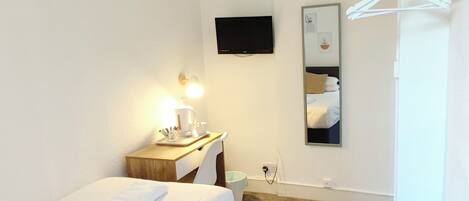 A hotel room with a bed, bedside table, lamp, TV, and a mirror.