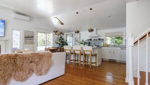 A spacious living area with a large sofa, wooden flooring, and a kitchen with white cabinets and a central island. - Luxe Lakefront Retreat★Sauna★Media Rm★Kayaks-SUPs★Bikes★Steps to BikePath★Pet OK (Harwich)
