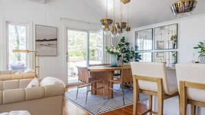 A modern living room with a sofa, dining table, chairs, and a large window. - Luxe Lakefront Retreat★Sauna★Media Rm★Kayaks-SUPs★Bikes★Steps to BikePath★Pet OK (Harwich)