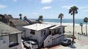 A two-story building with a flat roof, a garage, and a car parked in front. It is located near a beach with palm trees and the ocean in the background. - Manhattan Beach Beachfront Charming On The Strand (Manhattan Beach)