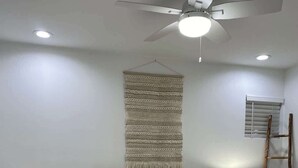 A bedroom with a bed, a bedside table, a lamp, a wall hanging, and a ceiling fan. - Manhattan Beach Beachfront Charming On The Strand (Manhattan Beach)