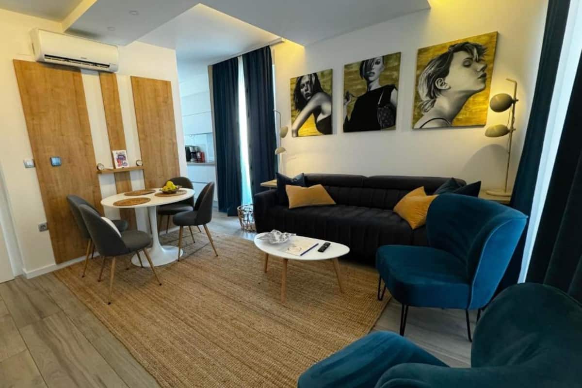 Un salon moderne avec un canapé noir, des fauteuils bleus, une petite table ronde et un coin repas comprenant une table et des chaises blanches.