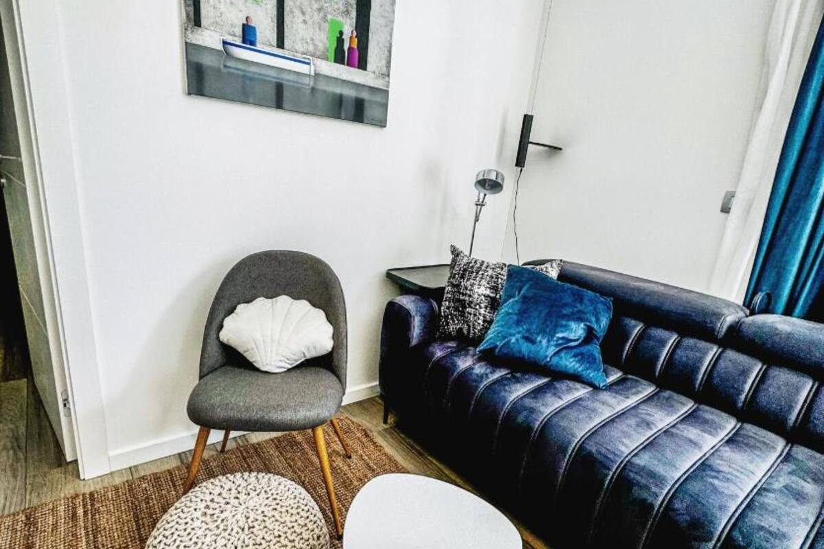 Un salon moderne avec un fauteuil gris, un canapé bleu agrémenté d’un plaid à motifs et une petite table ronde.