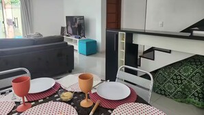 Uma sala de estar moderna com um sofá, uma televisão e um espaço de jantar com mesa posta para dois.