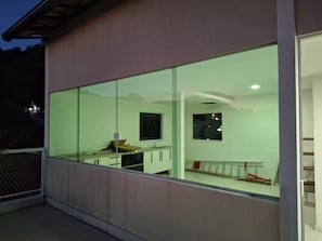 A modern building with large glass windows, a visible interior with a desk and chair, and a staircase leading to an upper level.
