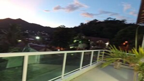 Varanda com grade de vidro e vista para uma região montanhosa com luzes distantes.