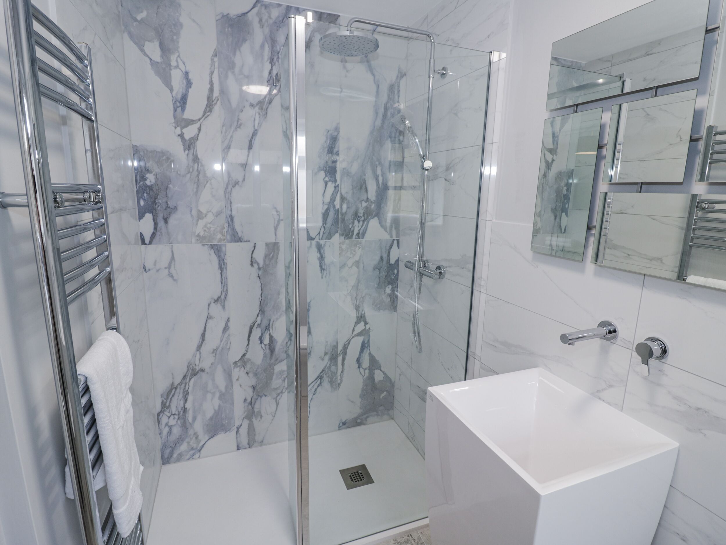 A modern bathroom with a glass-enclosed shower, a white sink, and a towel rack.