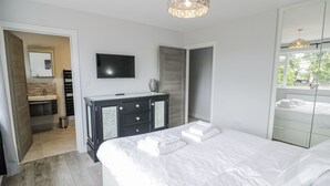 Ein modernes Schlafzimmer mit einem großen Bett, einem an der Wand montierten Fernseher, einer Kommode mit Schubladen und einem Spiegel.