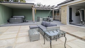 Eine Terrasse im Freien mit einem Tisch aus Glasplatten, gepolsterten Sitzmöglichkeiten und einem Whirlpool.