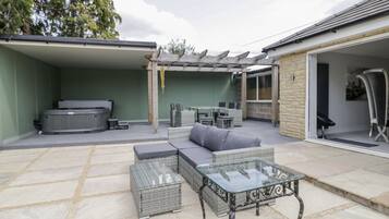 An outdoor patio area with a glass-top table, cushioned seating, and a hot tub.