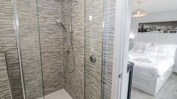 A modern bathroom with a glass-enclosed shower and a separate bedroom with a bed and a nightstand.