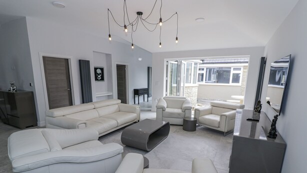 Ein modernes Wohnzimmer mit einem Ecksofa, Sesseln und einem Couchtisch. Ein großes Fenster lässt natürliches Licht herein und bietet einen Ausblick nach draußen.