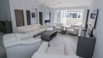 A modern living room with a sectional sofa, armchairs, and a coffee table. There is a large window providing natural light and a view of the outside.
