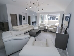 Una sala de estar moderna con un sofá modular, sillones y una mesa de centro. Hay un ventanal grande que proporciona luz natural y vistas al exterior.