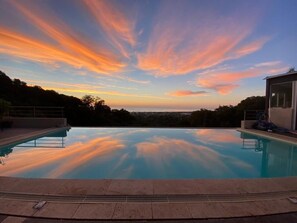 An infinity pool with a clear view of the sky and distant landscape. - Modern studio with magnificent sea view in a quiet, leafy setting (Furiani)
