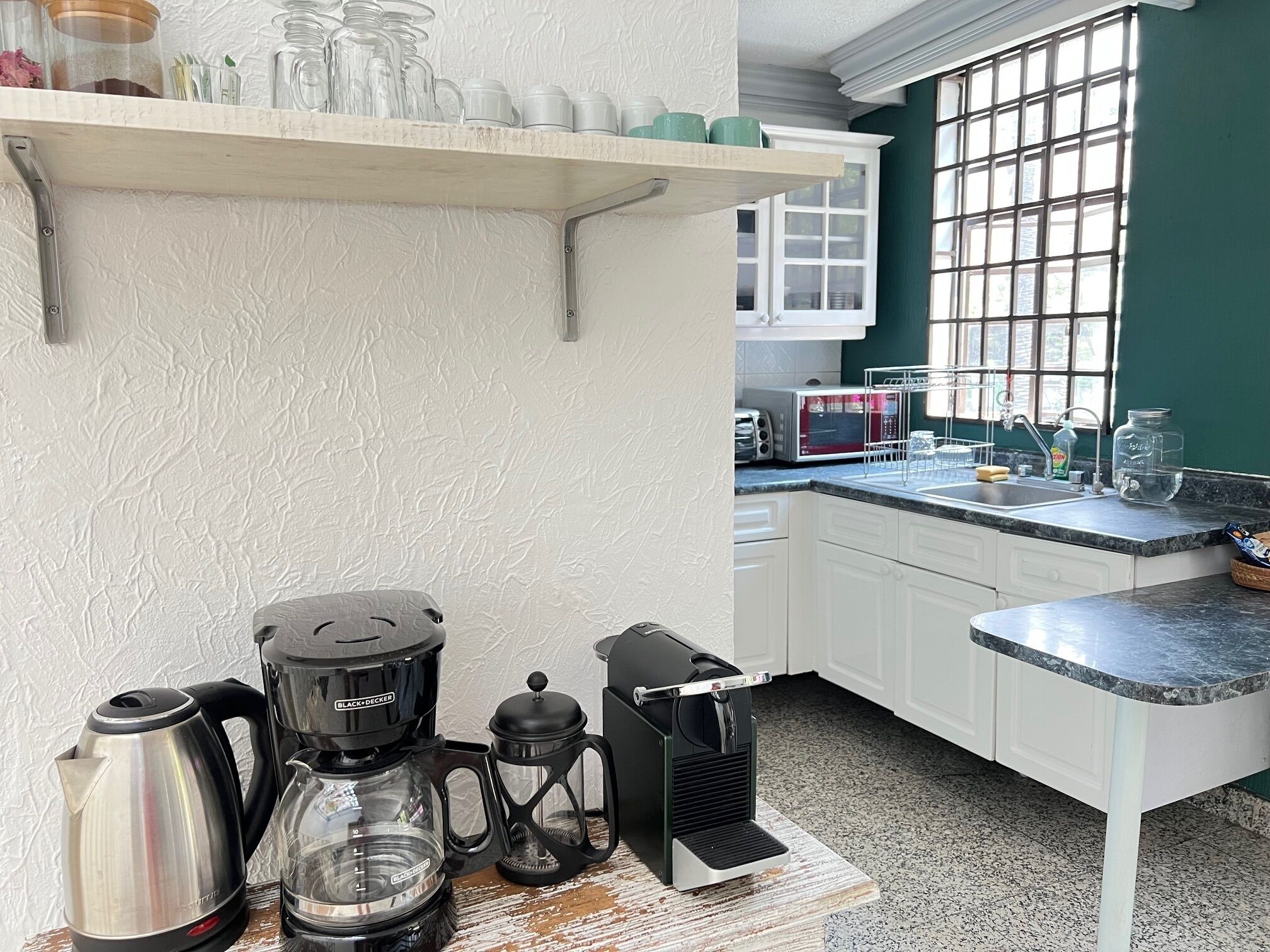 Una cocina con armarios blancos, encimera de granito, cafetera, hervidor y microondas.