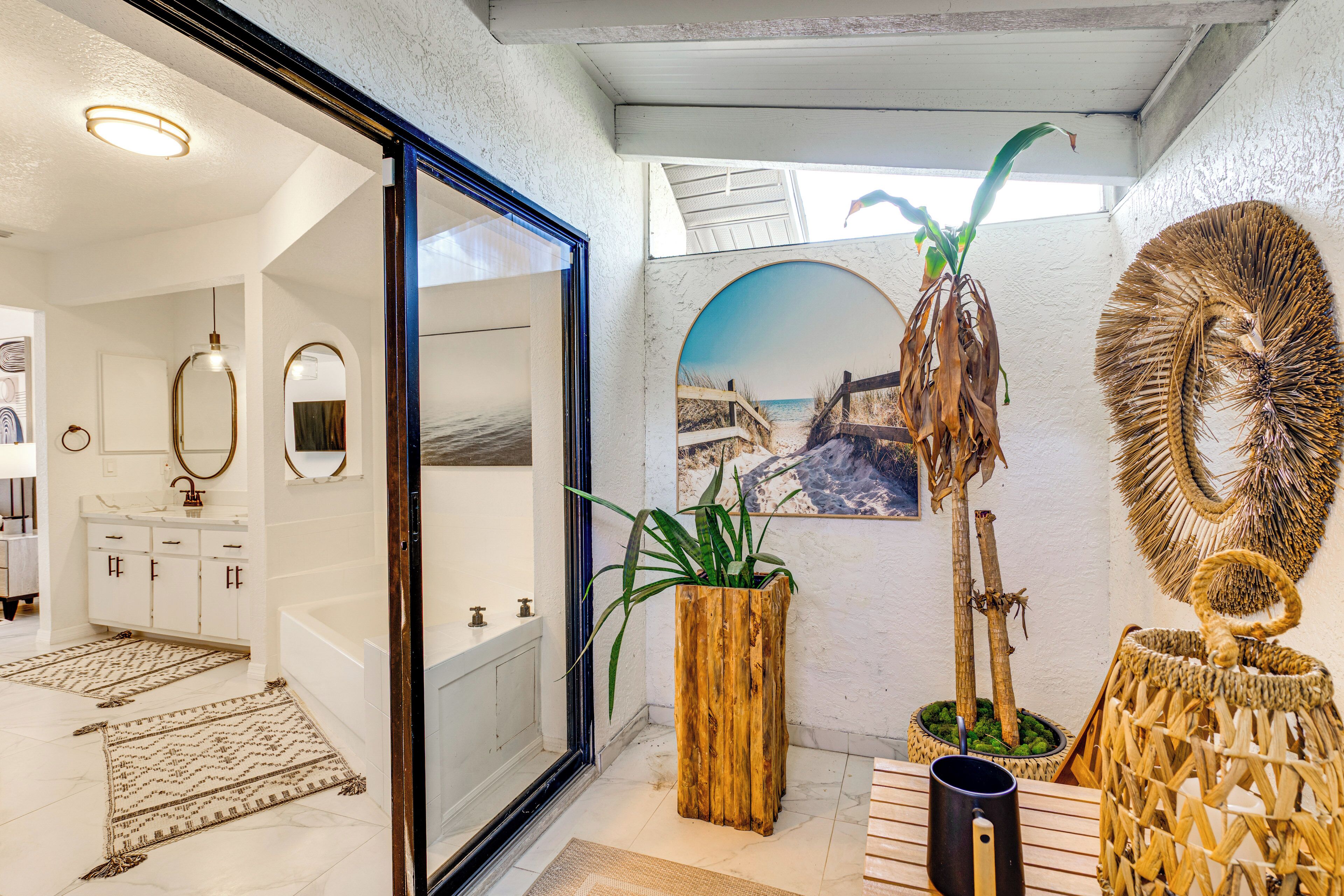 Une salle de bain moderne avec une baignoire, un grand miroir et un support à plantes en bois.