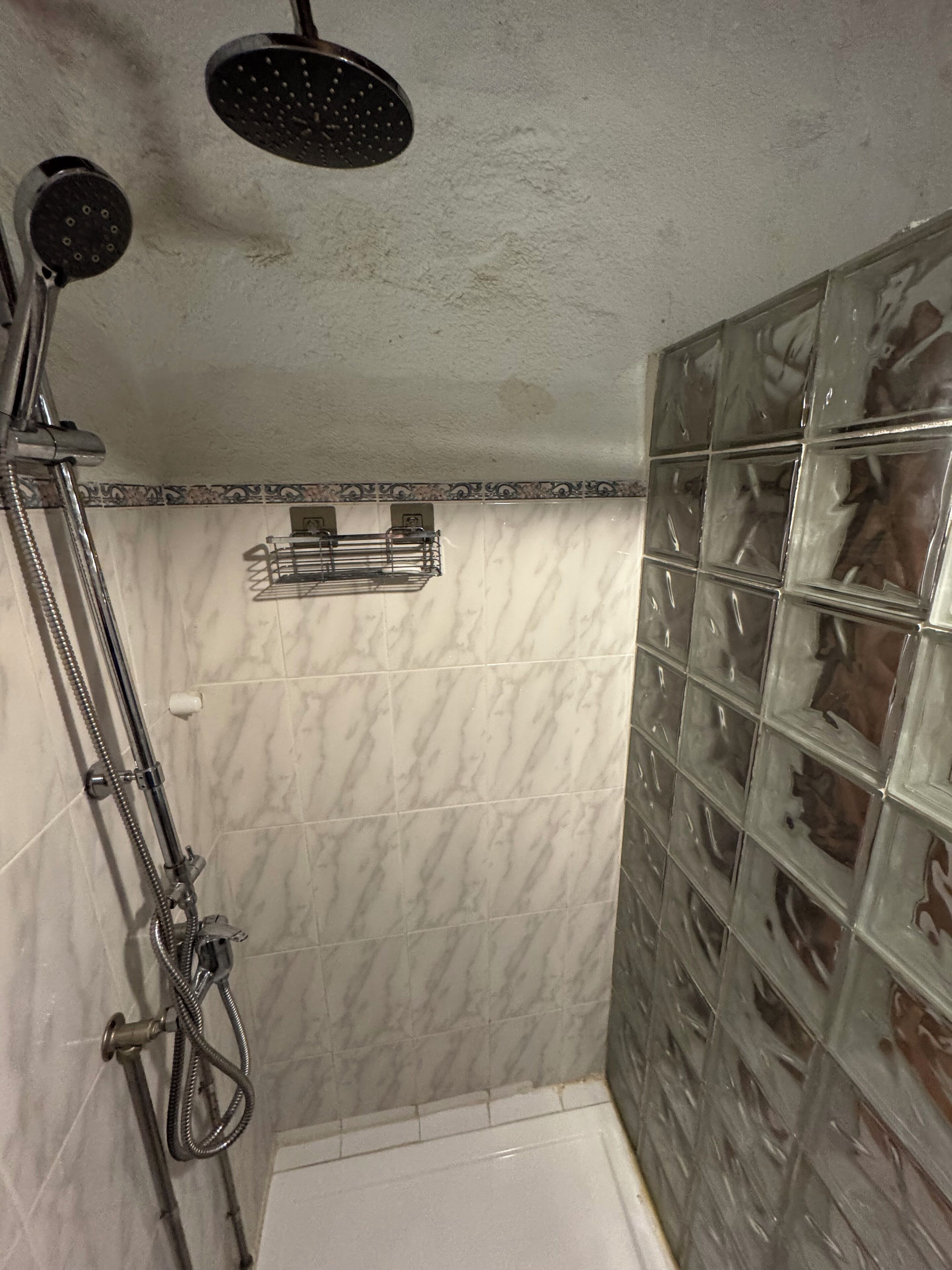 A shower with a handheld showerhead, a wall-mounted showerhead, and a glass shower enclosure.
