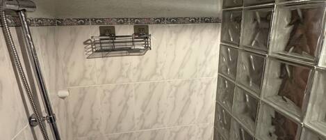 A shower with a handheld showerhead, a wall-mounted showerhead, and a glass shower enclosure.