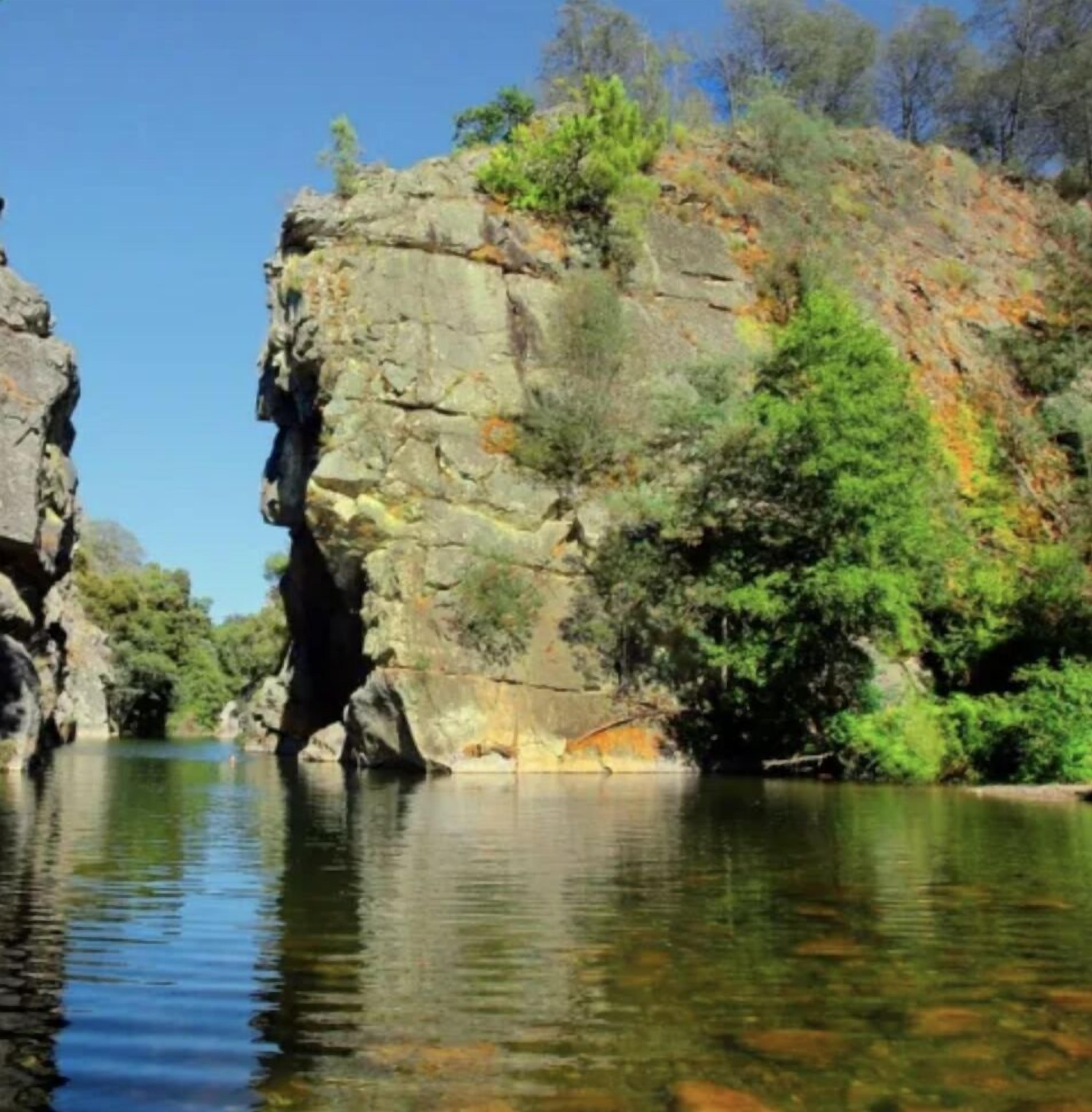 A natural landscape with a rocky cliff and a calm river.
