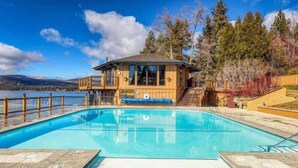 A wooden cabin with a pool, surrounded by trees and a lake.