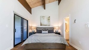 A bedroom with a large bed, a sliding glass door, a ceiling with exposed beams, and a wall-mounted artwork.