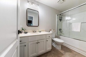 Un baño moderno con cabina de ducha de vidrio, un lavabo blanco con espejo y un inodoro.