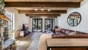 A spacious living room with a stone fireplace, wooden ceiling beams, a leather sofa, and a television.